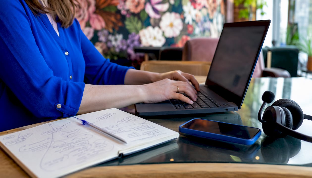 Detailopname van handen die typen op een laptop, met een headset op.